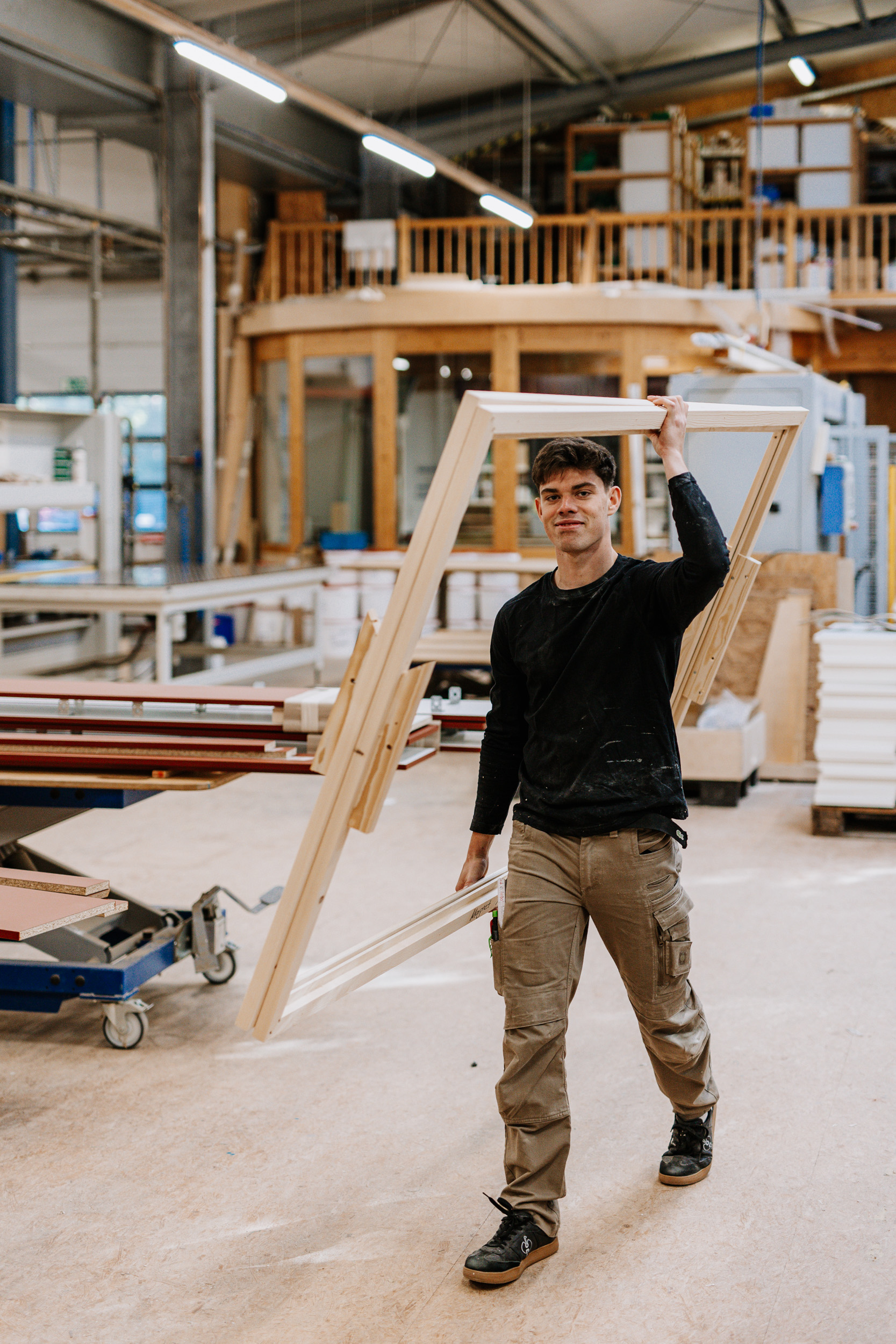 Ein Mitarbeiter trägt ein Holzgestell durch die Tischlerei.